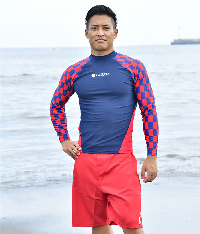 超撥水ラッシュガードを着用した男性が海辺に立っている。