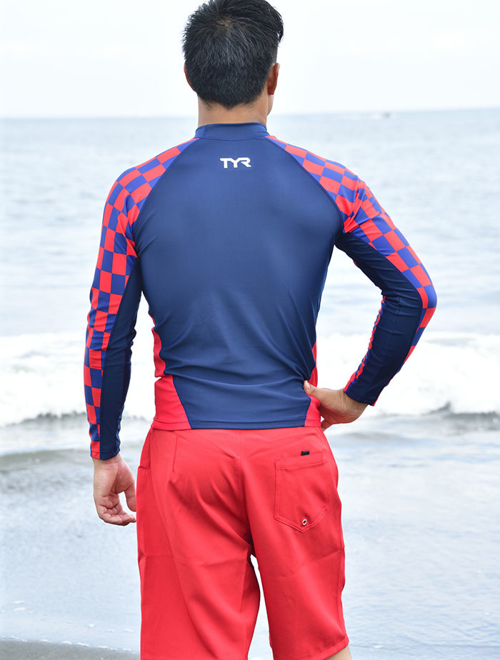 超撥水ラッシュガードを着用した男性が海辺に立って海を見ている